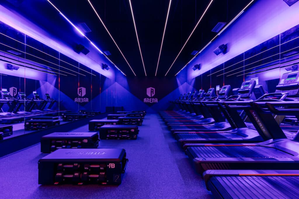 Ten treadmills fill the right hand side a nd 10 weight benches fill the left hand side of a purple-lit studio, with "Arena" written on the back wall.