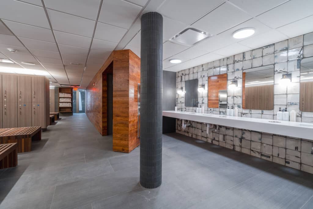 A locker room, with multiple vanities, lockers, towels and benches is shown.